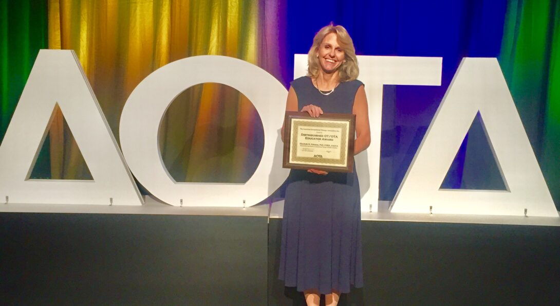 Liz Peterson stands holding her award certificate from AOTA