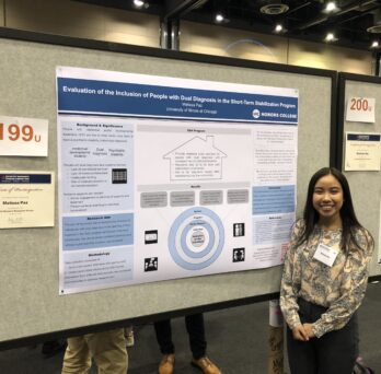 Melissa Paz stands before her research poster
                  