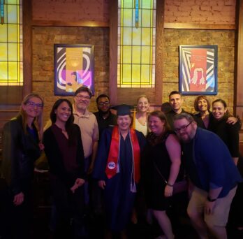 Noreen Chap wears her commencement regalia and is surrounded by a group of colleagues and friends.
                  