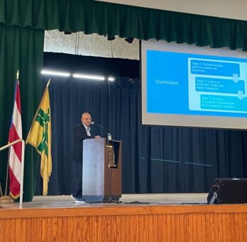 Carlos Crespo stand on a stage behing a podium while delivering a presentation
                  