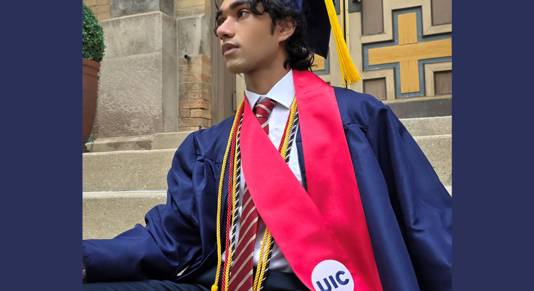 Student sits on outdoor steps wearing a navy graduation cap and gown, gold honor cords, and a red UIC stole.