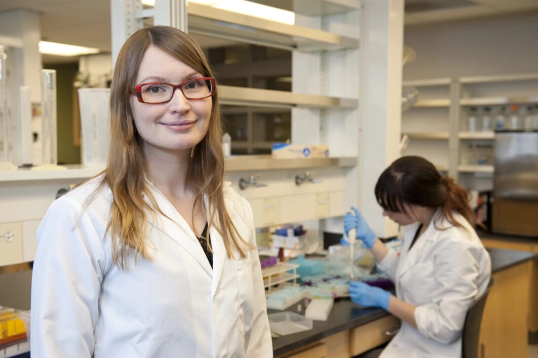 Krista Varady wears a white lab coat while standing in a research laboratory