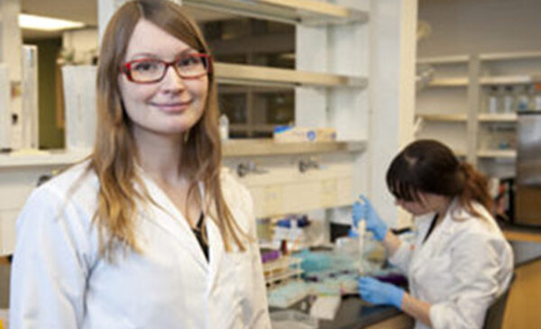 Woman stands in laboratory wearing a white lab coat