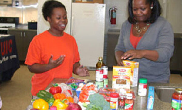 Two women stand around a kitchen counter filled with a variety of food