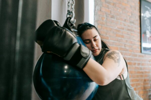 Woman wearing boxing gloves hugging boxing bag