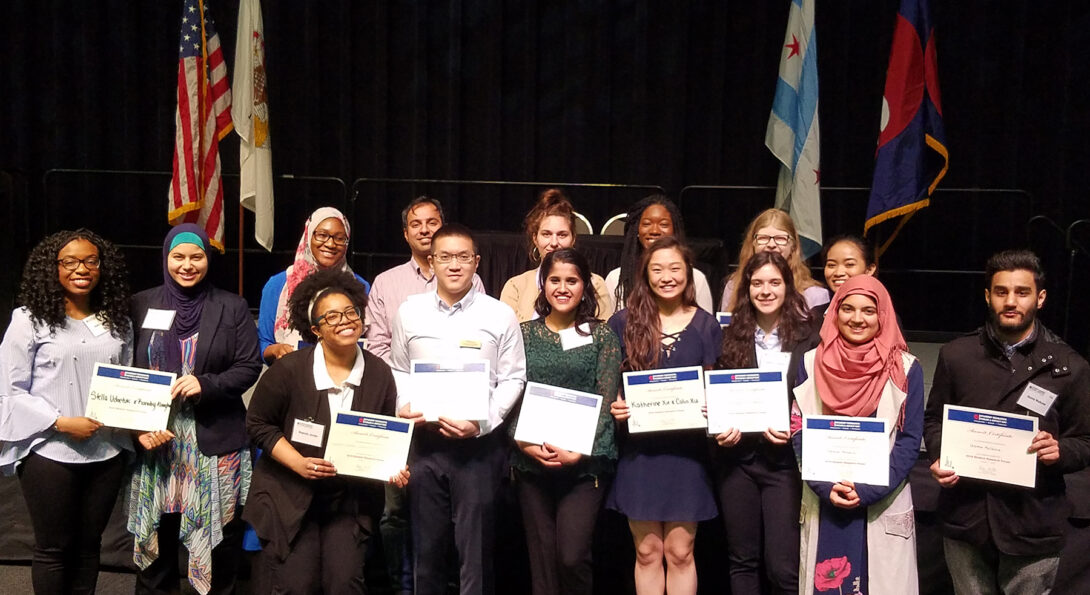 A group of fifteen student winners stand in two rows holding their award certificate