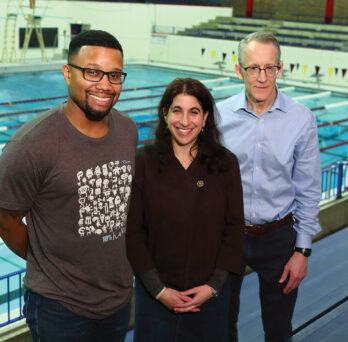 Jarrad Hampton-Marcell, Rachel Poretsky and Craig Horswill (from left to right) stand in front of an indoor swimming pool
                  