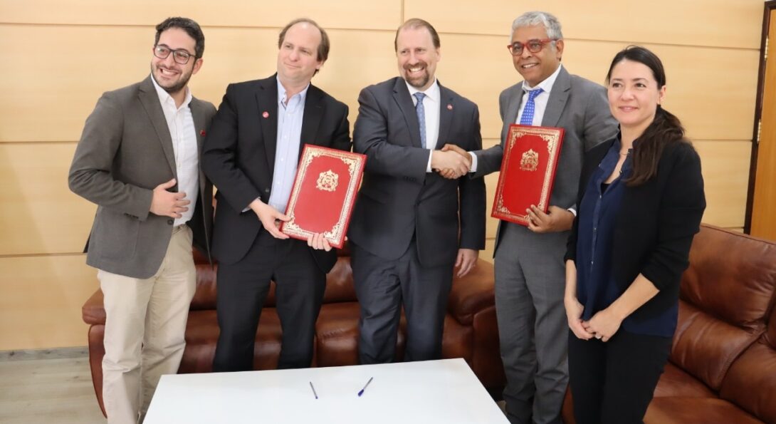 A group of five individuals stand holding two copies of the UIC University of Mohammed Premier agreement