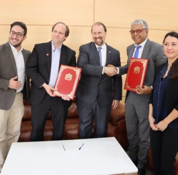 A group of five individuals stand holding two copies of the UIC University of Mohammed Premier agreement
                  