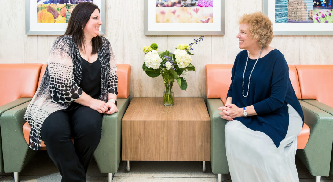 AnnaMaria Baraglia and Carol Gottlieb smile at each other while sitting next to one another