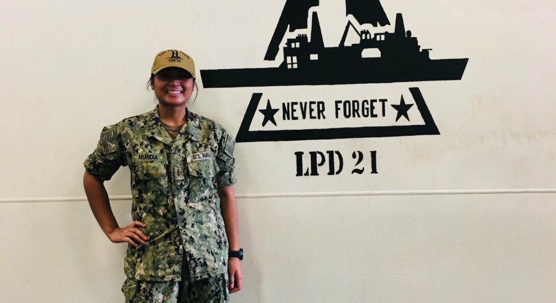 Genelle Arandia stands next to a large logo of the USS New York