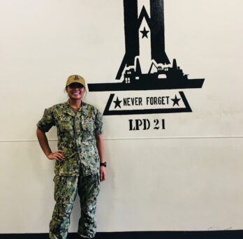 Genelle Arandia stands next to a large logo of the USS New York
                  