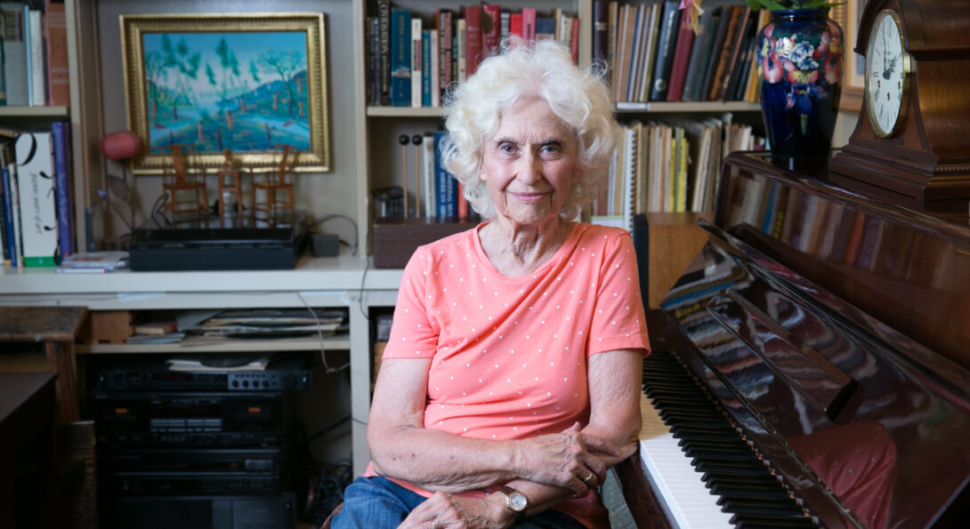 Phyllis Bowen sits next to a piano in her home library