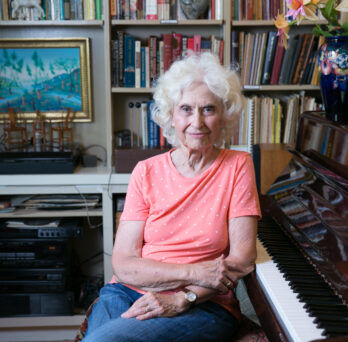 Phyllis Bowen sits next to a piano in her home library
                  