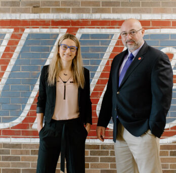 Karrie Hamstra-Wright and John Coumbe-Lilley standing in front of brick wall with UIC logo
                  