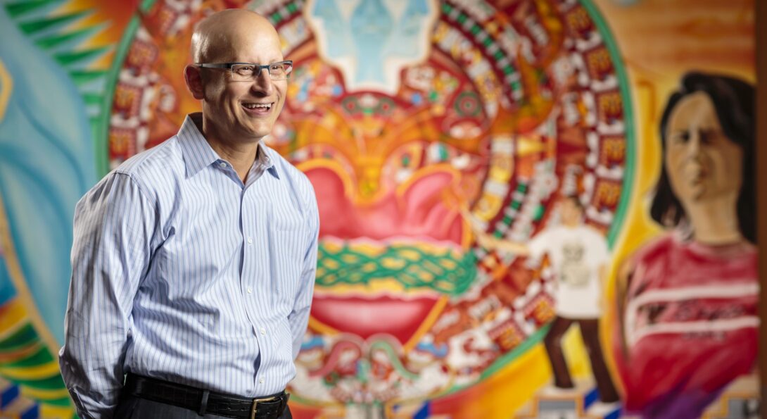 Carlos Crespo stands in front of a colorful wall mural