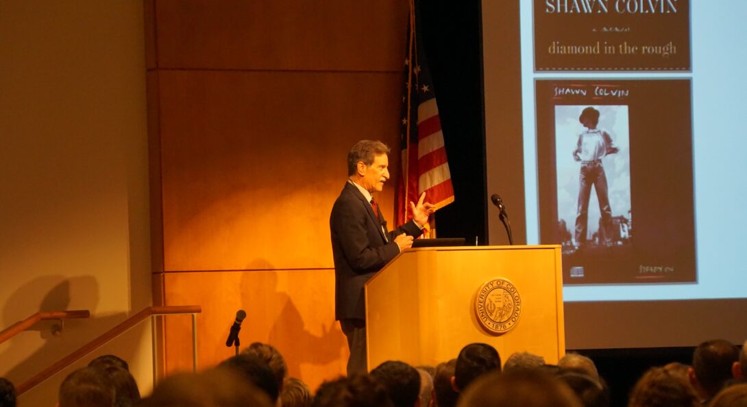 Grabiner stands behind a podium as he is addressing a seated crowd