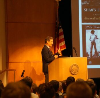 Grabiner stands behind a podium as he is addressing a seated crowd
                  