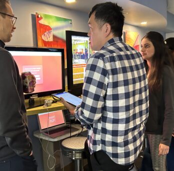 A group of AHS students and researchers gather around a screens to view demonstration.
                  