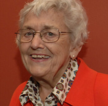 A head shot of a smiling Barbara Loomis against a bright red backdrop
                  