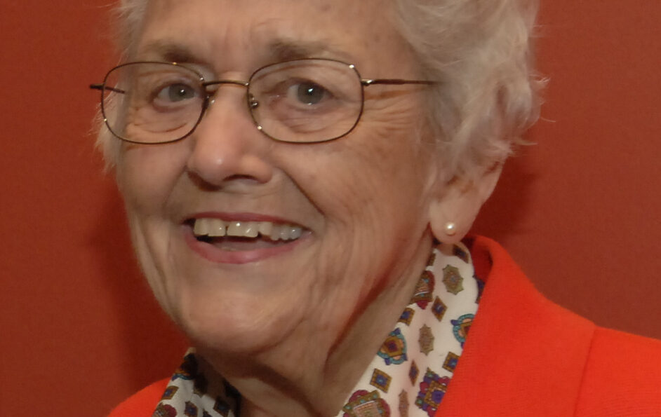 A head shot of a smiling Barbara Loomis against a bright red backdrop