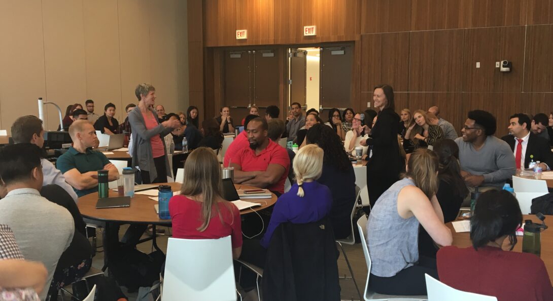 Tina Chase leading the post-role playing exercise discussion in a room full of students sitting around round tables