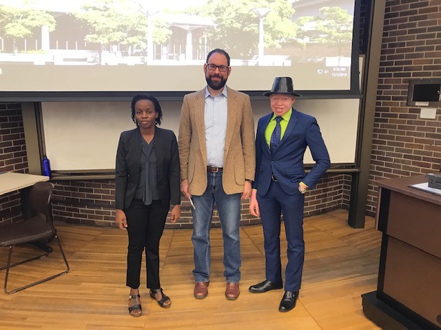 Esther Allen Nakamwa, Rob Gould and Peter Ogik standing together in front of a classroom whiteboard/projection screen