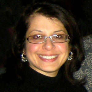 Head shot of smiling Rooshey Hasnain wearing a black turtle neck and eye glasses.
                  