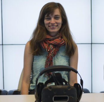 Carrie Shaw '16 MS BVIS stands behind a We Are Alfred virtual reality head gear
                  