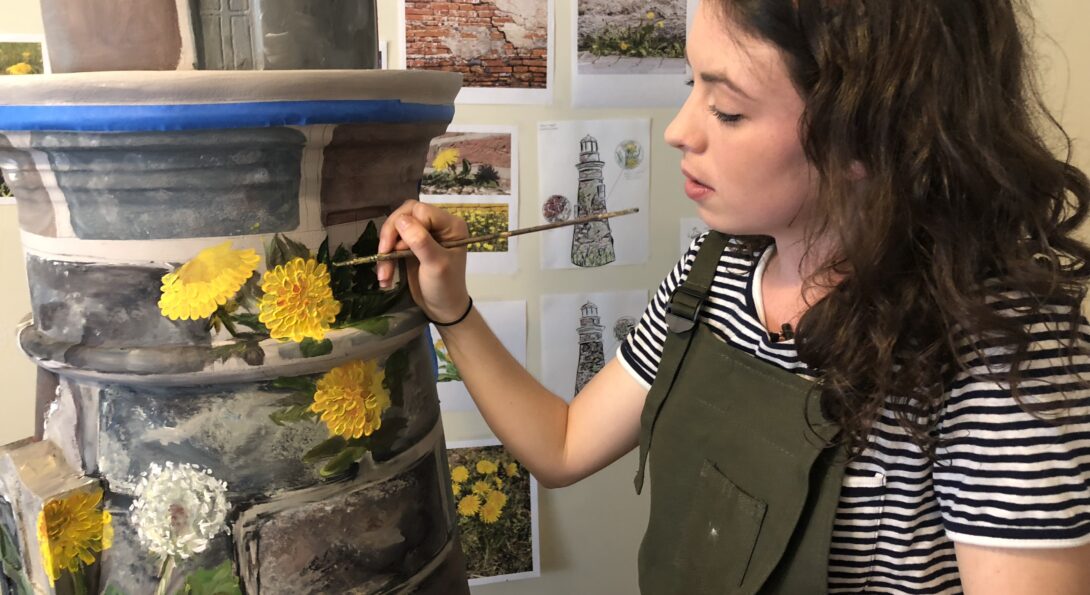 Kaitlin Stober paints yellow danelions on lighthouse sculpture