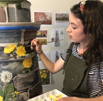 Kaitlin Stober paints yellow danelions on lighthouse sculpture
                  