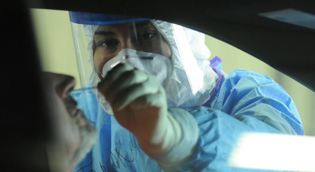 Akira Tanton administers a COVID-19 nasal swab test at a drive-in site