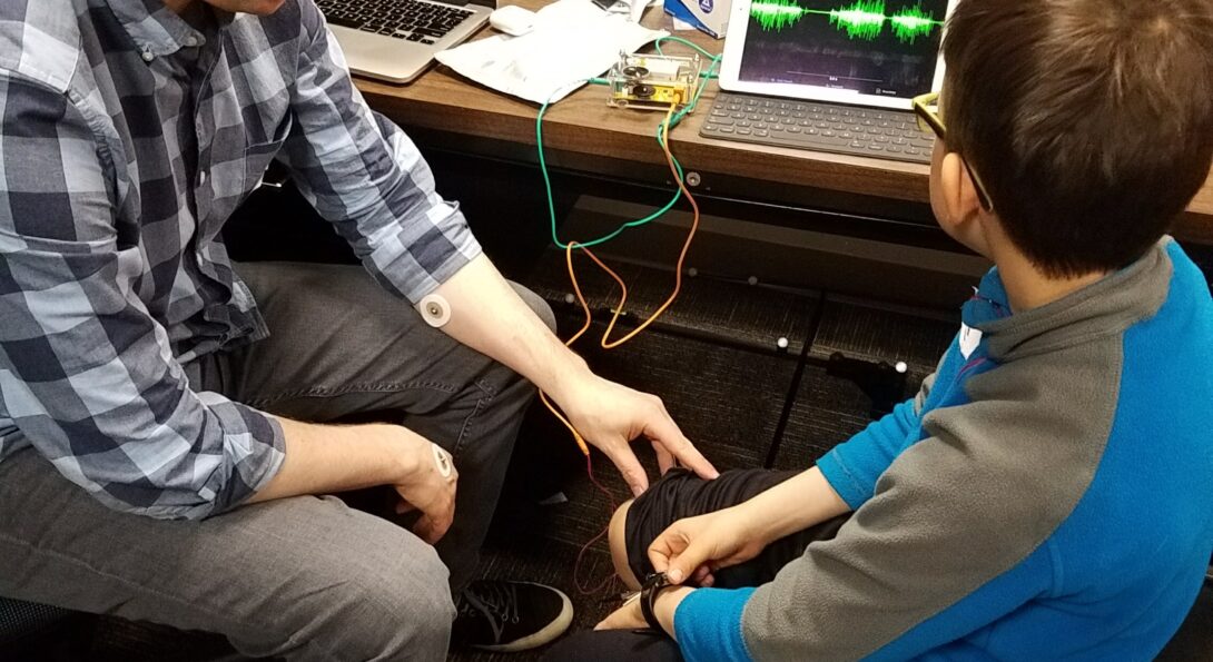 An AHS researcher and elementary school-aged student sit in front of health monitoring equipment