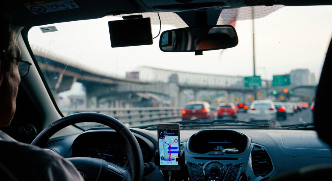 A photo from a car backseat perspective that shows a ride share drive behind the wheel of a car