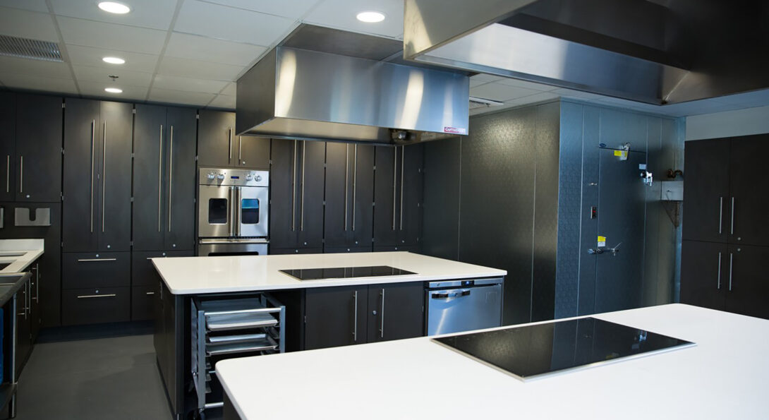 The Metabolic Kitchen containing stainless steel industrial kitchen appliances and white stone countertops