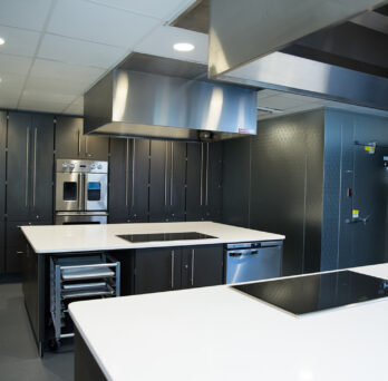 The Metabolic Kitchen containing stainless steel industrial kitchen appliances and white stone countertops
                  