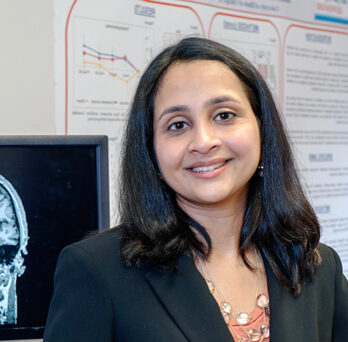 Sangeetha Madhavan in front of Brain Plasticity Lab equipment
                  