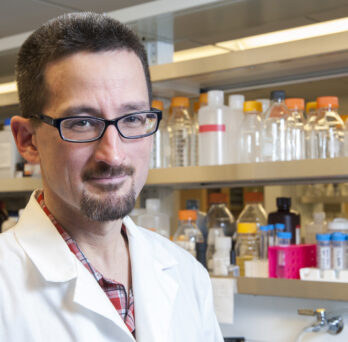 Timothy Koh wearing a white lab coat standing inside a research lab.
                  