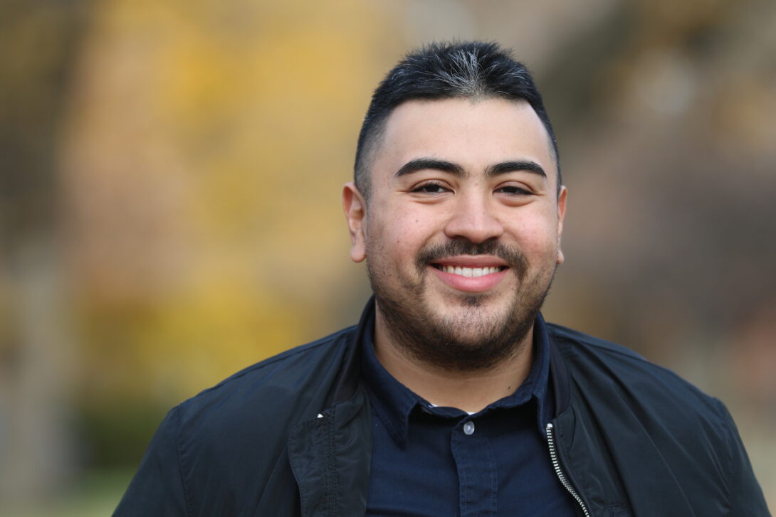 A smiling person in a dark jacket and dark shirt.