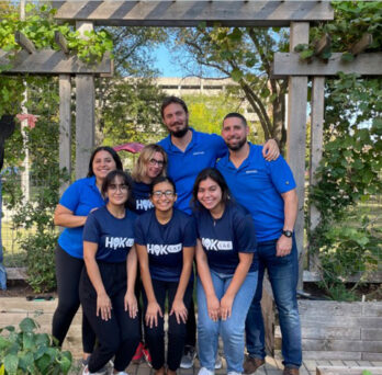 BUILT team wearing blue shirts posing together in the UIC teaching nutrition garden
                  