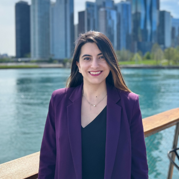Women in purple cut jacket smiling at the camera. Background is blurred laker and skyscrapers.