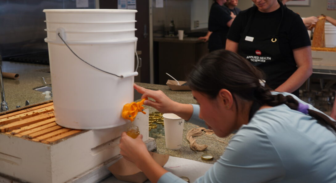 Sydney Galsan, UIC College of Liberal Arts and Sciences student, portions freshly extracted honey into jars while Renea Lyles looks on. Students received one-ounce samples to take home for their work during the harvest.