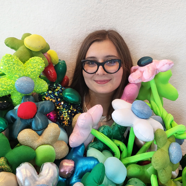 White women smiling at the camera wearing black cat eye glasses surrounded by plush green flowers.