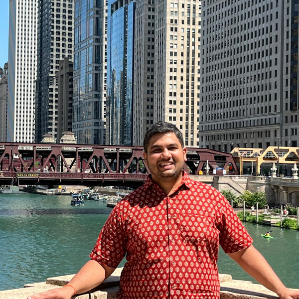Piyush smiling at the camera with skyscrapers and bridge in the background.