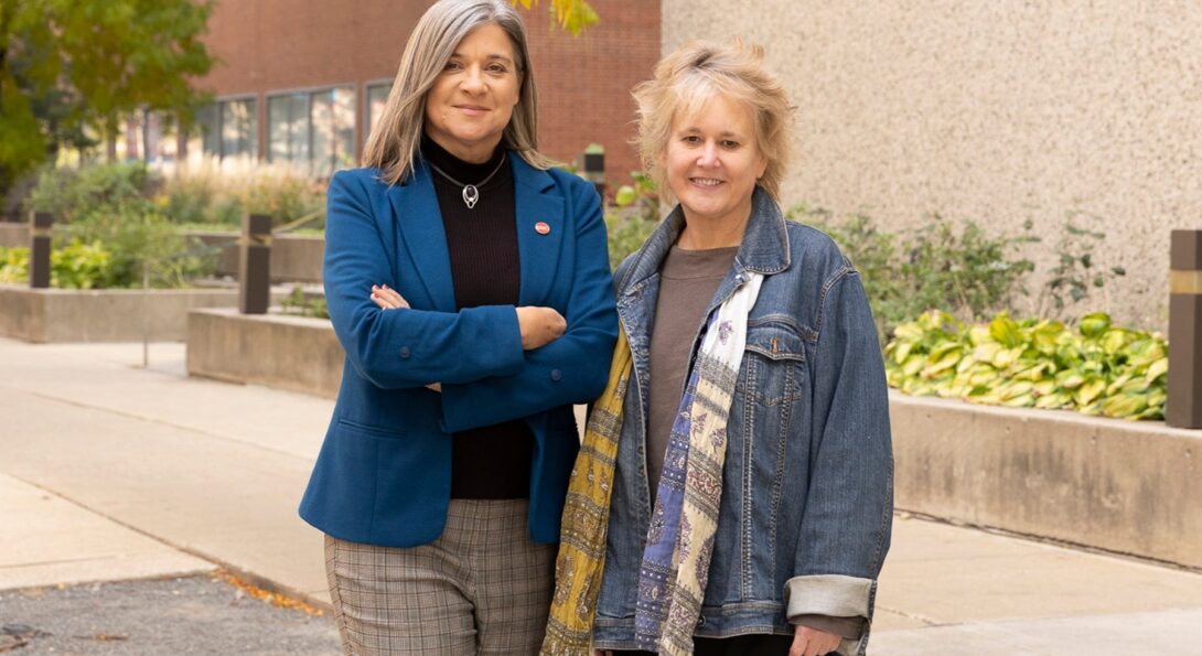 Susan Magasi and Joy Hammel stand next to each and outside on the west side of the UIC campus.