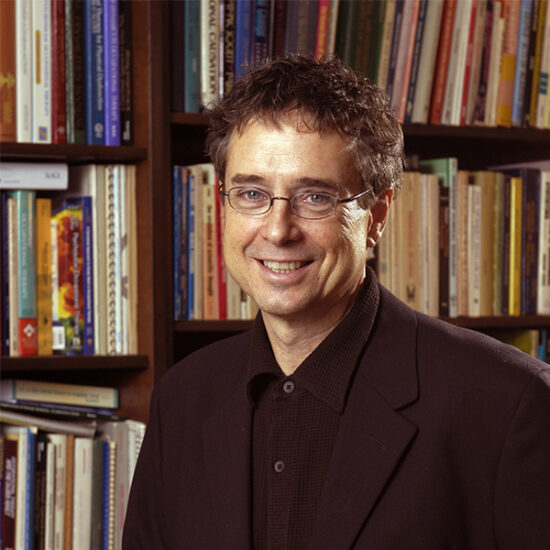 a man smiling at the camera with a bookshelf behind him full of books photo credit UIC Creative & Digital Services