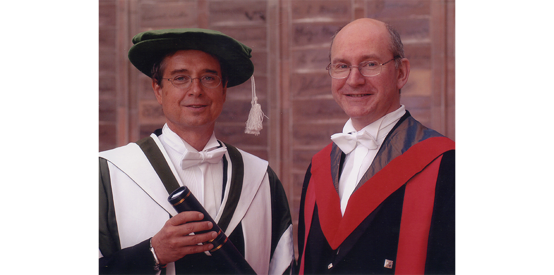 two men standing, wearing capes, smiling at the camera