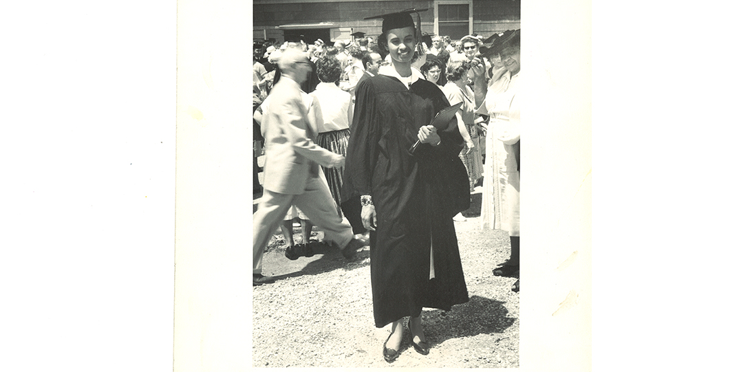 A black and white image of a woman in a black graduation gown