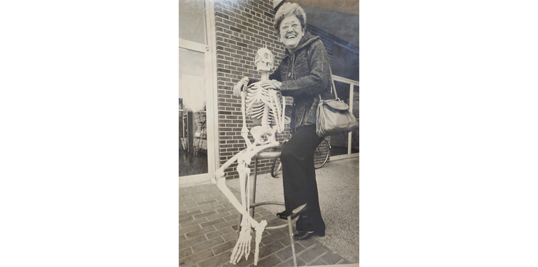 A black and white photo of a woman posing with a skeleton