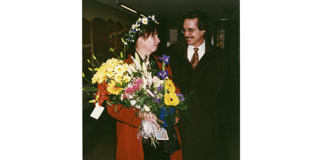 a woman standing holding a bouquet of flowers, and a man in a suit standing next to her smiling.